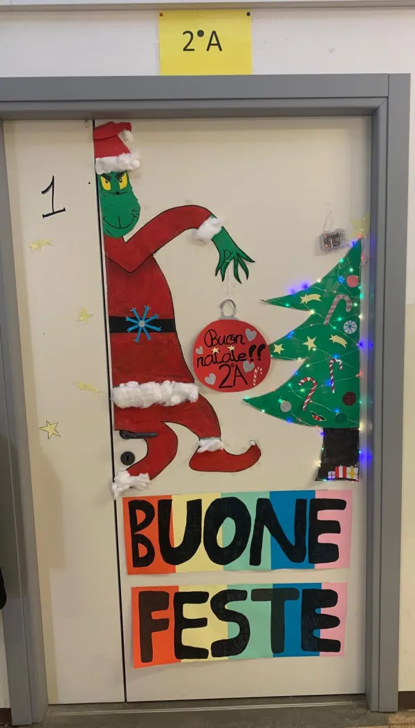 La porta di una classe decorata per Natale: un Grinch vestito da Babbo Natale, un albero e la scritta «Buone feste».